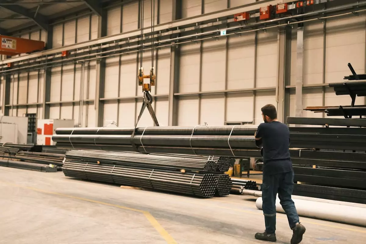 un-muncitor-manevreaza-cu-o-macara-pachete-de-tevi-din-otel-intr-o-hala