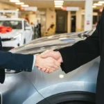 ce-sa-intrebi-dealerul-inainte-de-a-cumpara-o-masina-second-hand-iata-un-ghid-practic-si-util-dealer-auto-si-client-care-isi-strang-mainile-intr-un-showroom-cu-masini